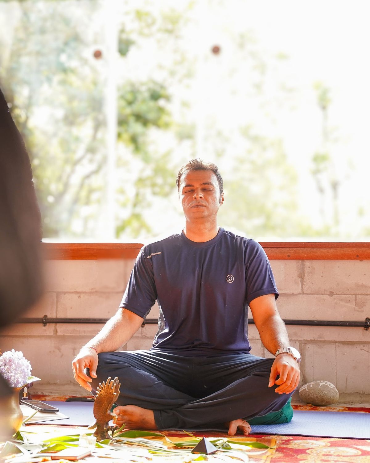 Vishal seated cross-legged on a mat in soft daylight, eyes closed, breathing